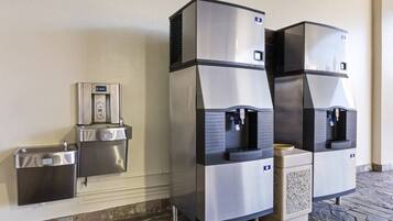 A water dispenser and trash bin mounted on a wall, with a stone-tiled floor.