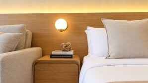 A hotel room with a wooden headboard, a bedside table with books, and a bed with white bedding. - Luxe Retreat – Modern Coastal Comfort (Honolulu)