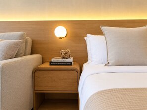 Una habitación de hotel con cabecera de madera, una mesita de noche con libros y una cama con ropa blanca.