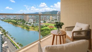A balcony with a view of a river and cityscape, furnished with a table and chairs. - Luxe Retreat – Modern Coastal Comfort (Honolulu)