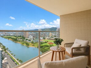 Un balcón con vistas a un río y un paisaje urbano, amueblado con una mesa y sillas.