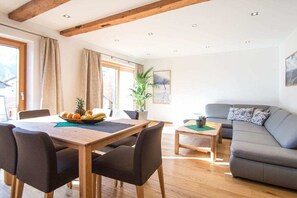 A room with a dining table, chairs, a sofa, and a small coffee table. - 60 m² Guesthouse Sonne (Bichlbach)