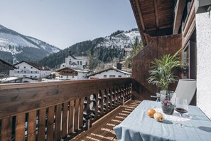 Ein Balkon mit Holzgeländer, einem Tisch mit Tischdecke, einem Blumentopf und einem Weinglas.