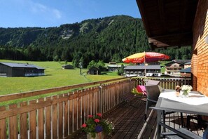 Een balkon met uitzicht op een bergachtig landschap, een houten omheining en buitenmeubels.