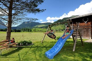 A playground with a slide and swings in a grassy area with a mountain backdrop. - Holiday apartment with 4 bedrooms (Schoppernau)