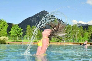 A person in a swimming pool with water splashing around them, surrounded by greenery and mountains in the background. - Holiday apartment with 4 bedrooms (Schoppernau)