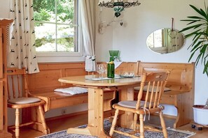 Ein Holzbänkchen und ein Tisch stehen in einem Raum mit Fenster, Spiegel und einer Topfpflanze.
