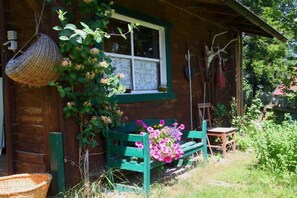 A wooden cabin with a window, a bench with flowers, and a hanging basket.