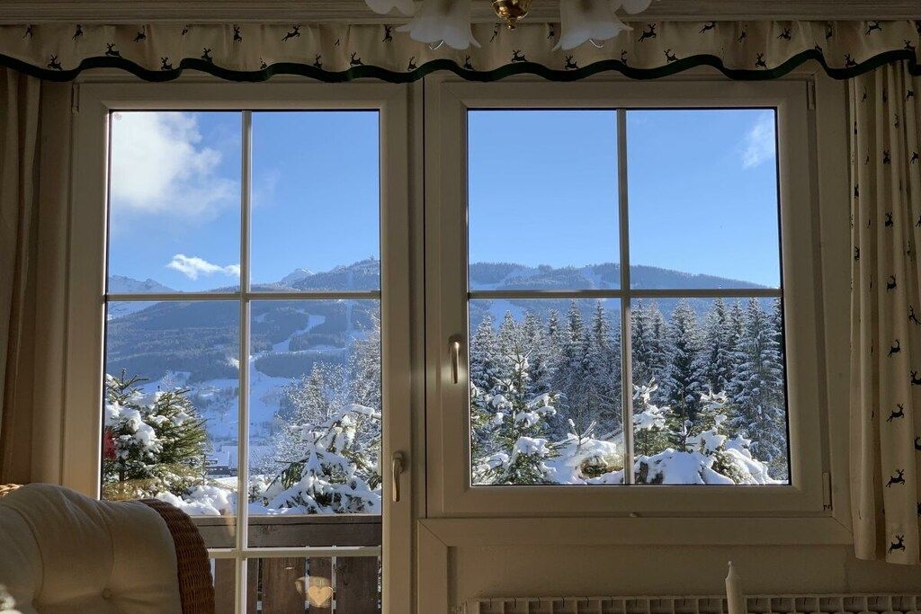 Une pièce dotée d’une grande fenêtre donnant sur un paysage enneigé, avec des arbres et des montagnes.