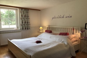 A bedroom with a bed, a bedside table with a lamp, a window with curtains, and a wall with a text.