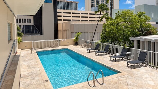 A rooftop pool with a clear blue pool, surrounded by lounge chairs and a white railing. - New Waikiki Studio | King | Parking | Pool (Honolulu)