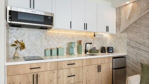 A modern kitchen with a built-in microwave, wooden cabinets, and a herringbone-patterned backsplash. - New Waikiki Studio | King | Parking | Pool (Honolulu)