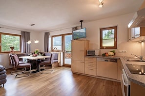A modern kitchen with a dining area, wooden cabinets, a built-in microwave, and a large window overlooking greenery. - Maple tree in Christina's country house (Mayrhofen)