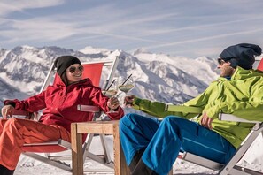 Zwei Personen sitzen auf Stühlen vor einer Bergkulisse.