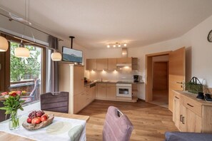 Eine moderne Küche mit Holzausstattung, ein Essbereich mit Tisch für zwei Personen und Blick ins Freie.