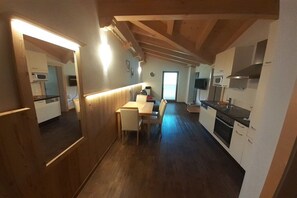 Een smalle gang die leidt naar een eetruimte met een tafel en stoelen, houten vloeren en een keuken met moderne apparatuur.