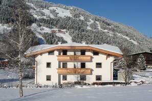 A two-story building with a balcony, surrounded by snow-covered trees and a mountain in the background. - Holiday home with 1 bedroom (Zell am Ziller)