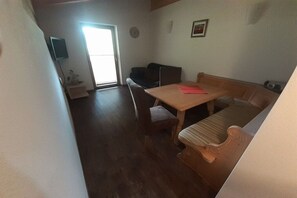 Ein Zimmer mit Holztisch, einer Couch, einem Fernseher und einer Tür zum Balkon.
