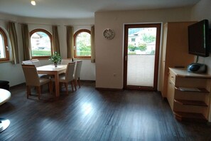 Ein Zimmer mit Esstisch, Stühlen, einem Fernseher und einer Schiebetür, die zu einem Außenbereich führt.