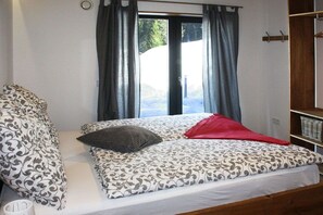 Ein Schlafzimmer mit einem Bett, einem Fenster mit Vorhängen und Blick ins Freie.