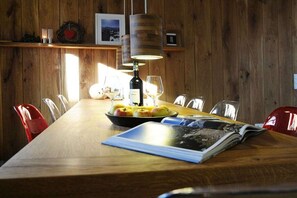 A wooden dining table with a bowl of fruit, a bottle, and glasses. - Holiday home in Riezlern with swimming pool (Riezlern)
