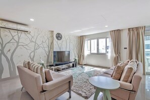 A modern living room with a sofa set, a glass coffee table, a flat-screen TV, and a decorative wall with tree patterns. - Pratumnak Hill 2BR Sea View (PH3) (Banglamung)