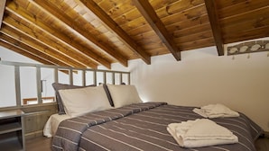 A bedroom with a wooden ceiling, a bed with striped bedding, and a nightstand. - Kaminos Boutique Hotel (Symi)