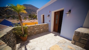 A building with a stone-paved entrance, a palm tree, and a mountain in the background. - Kaminos Boutique Hotel (Symi)
