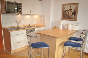 A kitchen with white cabinets, a microwave, a sink, and a coffee maker. There are two blue bar stools and a framed picture on the wall. - 08 Heringsdorf Lake Castle (Heringsdorf)
