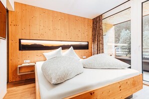 Ein modernes Schlafzimmer mit einem Holzkopfteil, einem großen Bett mit weißer Bettwäsche und Blick ins Freie durch eine Glastür.