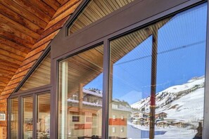 Un bâtiment moderne doté de grandes fenêtres, d’un plafond en bois et offrant une vue sur un paysage montagneux enneigé.