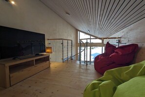 Un intérieur moderne avec un grand téléviseur à écran plat posé sur un meuble en bois, un fauteuil en forme de poire rouge et un autre, vert.