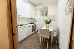 A compact kitchen with white cabinets, a stove, and a dining table with chairs. - A spacious and bright 87-square-meter apartment perfect for six people, located on the first floor of a building (equipped with an elevator, though there are a few steps to reach it; NOT suitable for people with disabilities).The property is centrally lo (Rome)