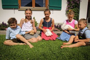 Four children sitting on grass in front of a building with a window and a flower box. - in the Bergquell house with horse stable (Au, Bregenzerwald)