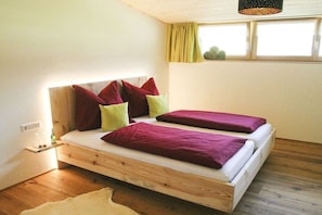 A room with a wooden bed, two pillows, a bedside table, and a window with curtains. - in the Bergquell house with horse stable (Au, Bregenzerwald)