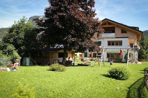 A two-story building with a balcony, surrounded by a grassy area and trees. - in the Bergquell house with horse stable (Au, Bregenzerwald)
