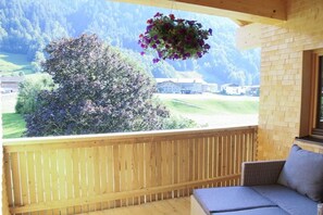 A wooden deck with a view of a mountain landscape, a hanging flower basket, and a cushioned seating area. - in the Bergquell house with horse stable (Au, Bregenzerwald)