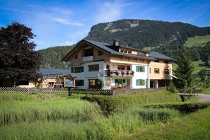 A two-story building with a balcony, surrounded by a fence, and a mountain in the background. - in the Bergquell house with horse stable (Au, Bregenzerwald)