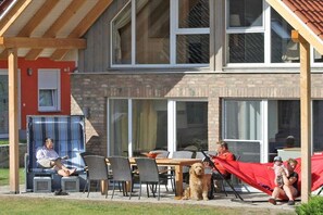 A building with a brick facade, large windows, and a covered outdoor seating area with chairs and tables. - Holiday home with 5 bedrooms (Röbel an der Müritz)