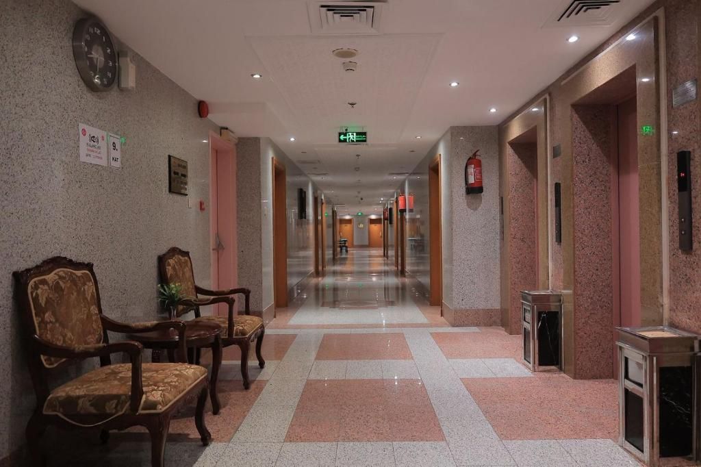 Een hotel lobby met een lange gang, houten stoelen, een brandblusser en een nooduitgangbord.