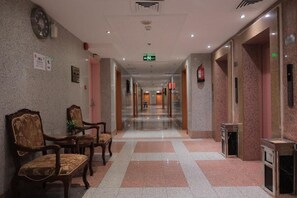 A hotel lobby with a long corridor, wooden chairs, a fire extinguisher, and an emergency exit sign. - Al Qimah Atlas Hotel (Makkah)