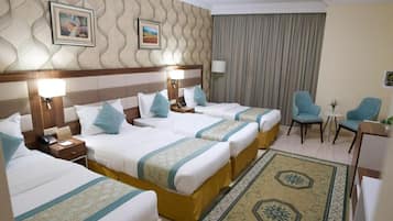 A hotel room with four beds, a sitting area with two chairs, a small table, and a decorative rug.