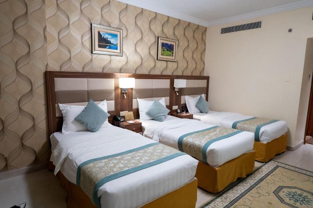 A hotel room with three beds, each with a headboard, bedside tables, and lamps.
