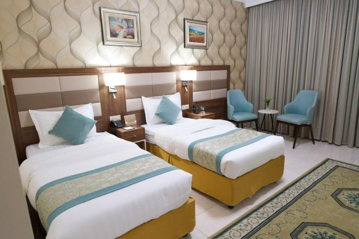 Habitación de hotel con dos camas, una mesita, dos sillas y una alfombra decorativa.