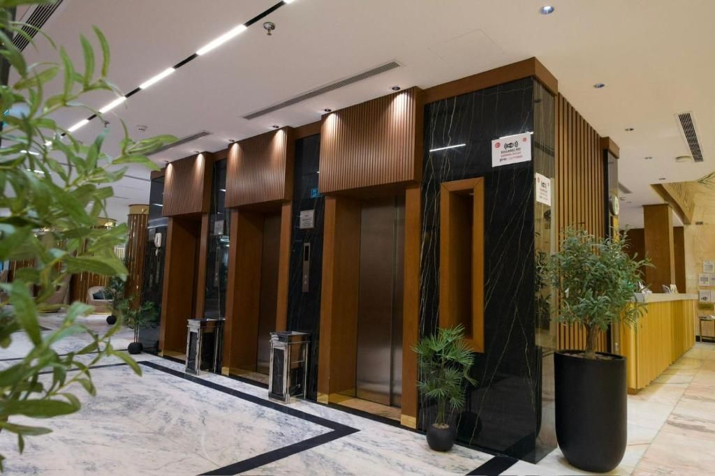 Un vestíbulo de hotel con mostrador de recepción, ascensores y plantas en macetas.
