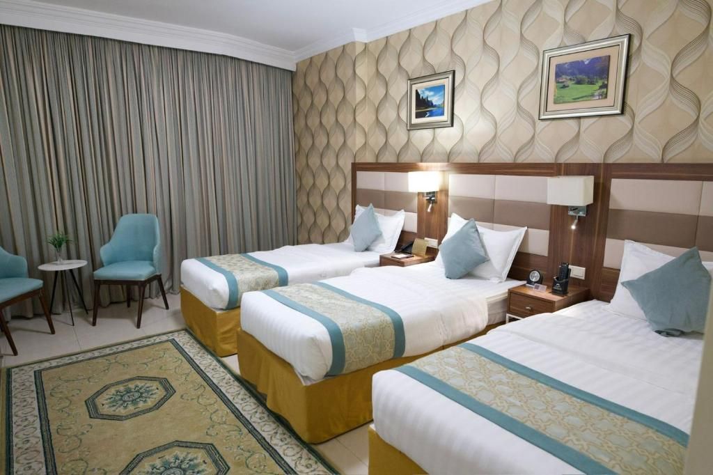 Una camera d'albergo con due letti, un tavolino, una sedia e un tappeto decorativo.