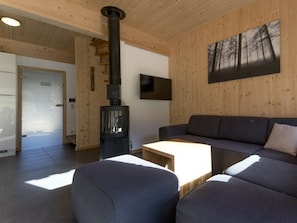 A modern interior with a wood-burning stove, a sofa, and a painting of trees. - One-bedroom Cabin (Sankt Georgen am Kreischberg)