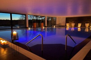 Une piscine avec vue sur l’extérieur, un fauteuil de relaxation et des bougies.