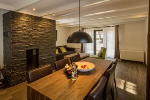 Un salon moderne avec une cheminée en pierre, une table à manger avec des chaises et un grand luminaire suspendu noir.