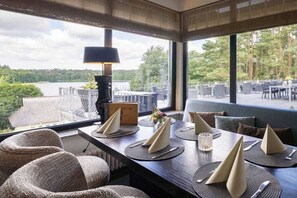 A dining area with tables set for two, a view of a lake, and outdoor seating. - Holiday apartment with 1 bedroom (Nossentiner Hütte OT Drewitz)